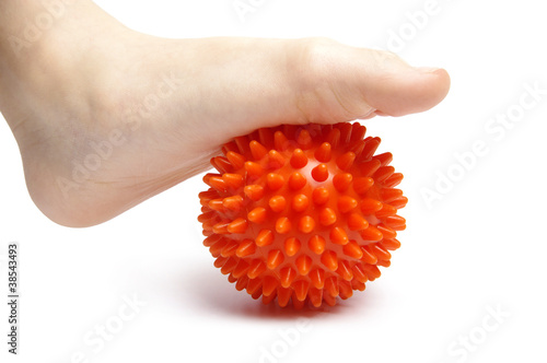 Child foot with spiny plastic orange massage ball on white backg
