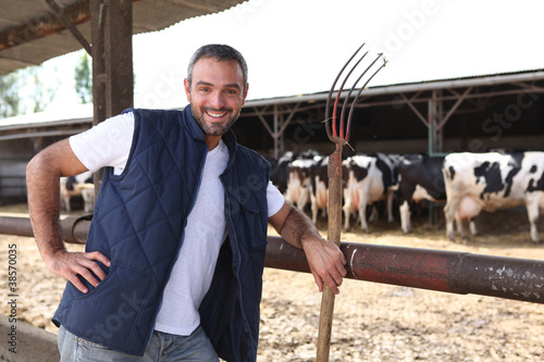 Canvas-taulu farmer with a hayfork in front of cowshed
