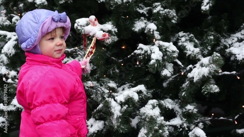 girl stands and hold bow ribbon on Christmas tree photo