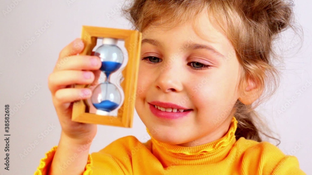 Little girl hold sand glass in wooden frame and tell something Little girl hold sand glass in wooden frame and tell something