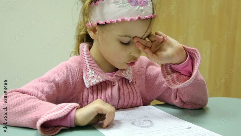 Little girl sits at table with piece of paper and reads test Little girl sits at table with piece of paper and reads test