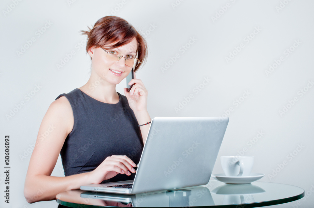 Smiling young business woman speaking on mobile phone while usin Smiling young business woman speaking on mobile phone while usin