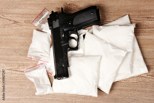 Fotografie Cocaine in packages and handgun on wooden background