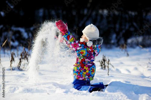 Toddler girl in colorful snowsuit plays in snow photo