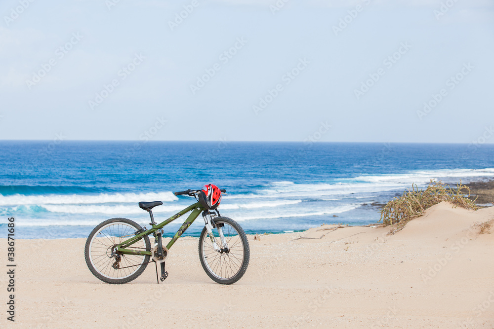 Bicycle with helmet, stand on the beach.