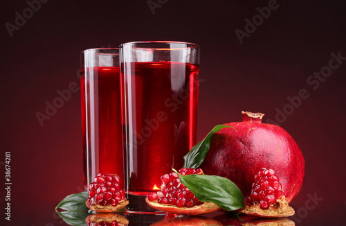 ripe pomergranate and glasses of juice on red background photo