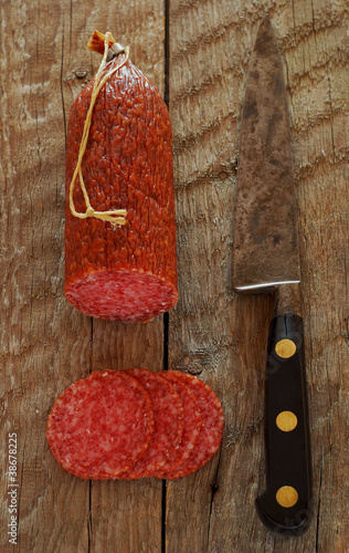 Salami with slices on rustic wood with an old knife