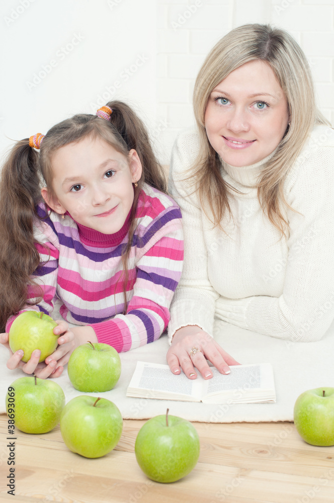 Fototapeta premium Smiling mom and her daughter lying on the floor with a book