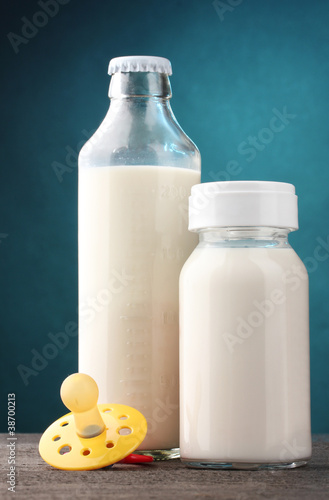 bottles of milk and soother on wooden table on blue background