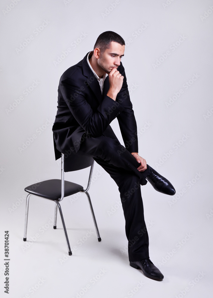 Elegant young businessman sitting on a chair and thinking - obrazy, fototapety, plakaty 