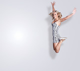 Young beautiful blond woman jumping in air on a gray background