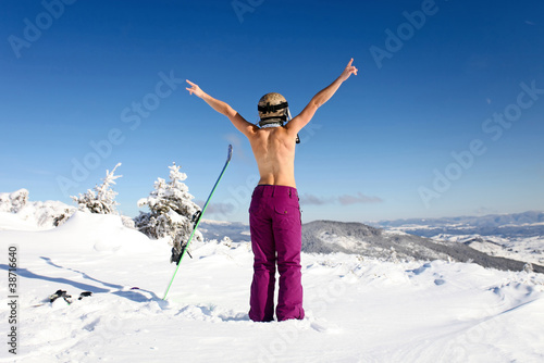 Rear view of female skier posing topless on mountain slope