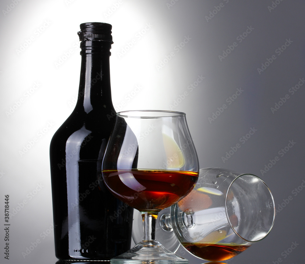 Glasses of brandy and bottle on gray background Glasses of brandy and bottle on gray background