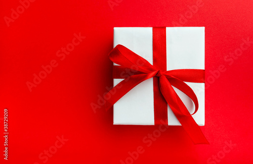 Small gift with red bow on red background.