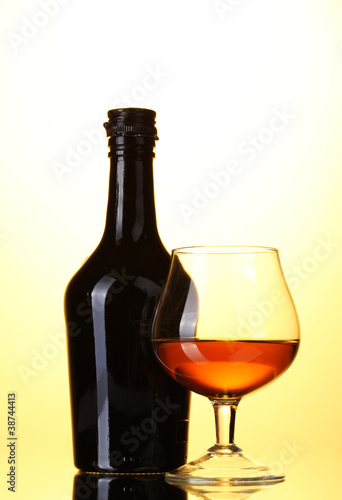 Glass of brandy and bottle on yellow background