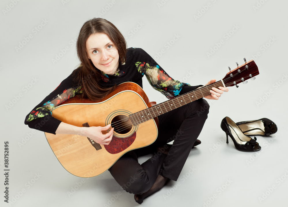Attractive brunette girl playing guitar sitting on the floor