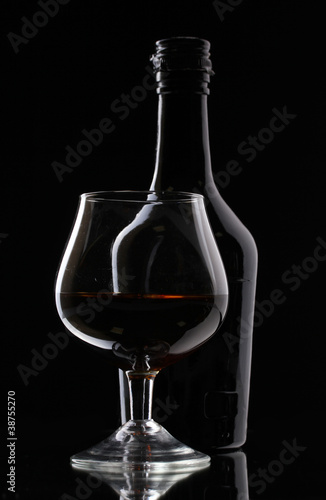 Glass of brandy and bottle on black background