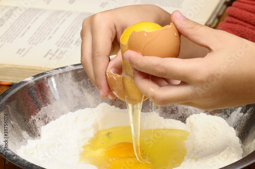 Child's hand breaking egg into flour and recipe book photo