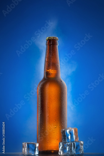 Cold beer bottle with drops, frost and vapour on blue