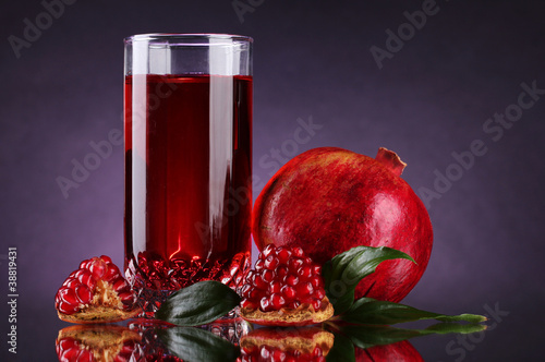 ripe pomergranate and glass of juice on purple background photo