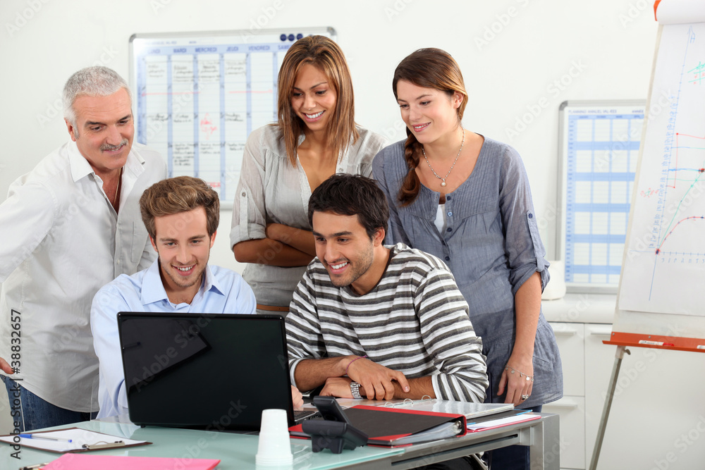 Co-workers gathered around computer screen Co-workers gathered around computer screen