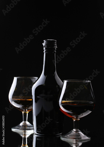 Glasses of brandy and bottle on black background