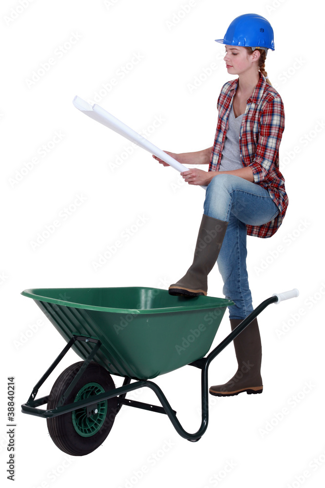 craftswoman leaning on a wheelbarrow looking at a blueprint craftswoman leaning on a wheelbarrow looking at a blueprint