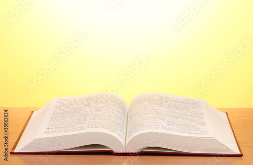 Open book on wooden table on yellow background