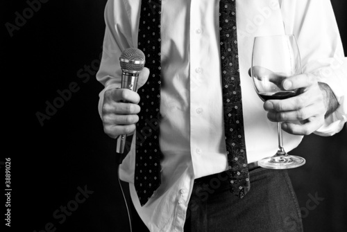 Man with untucked shirt holding a drink and a microphone