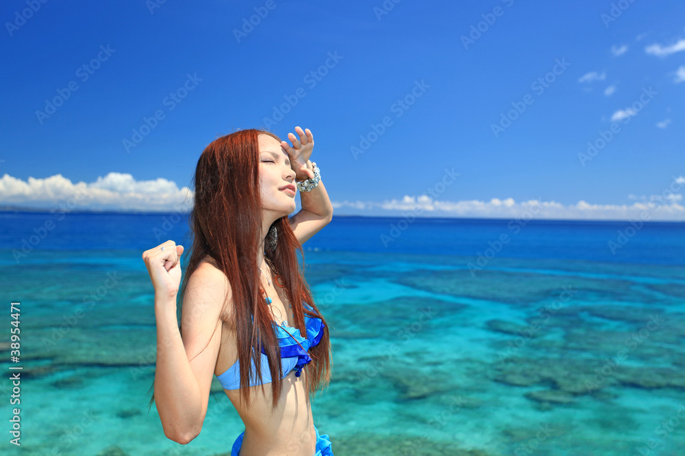 眩しそうに空を見上げる水着姿の女性