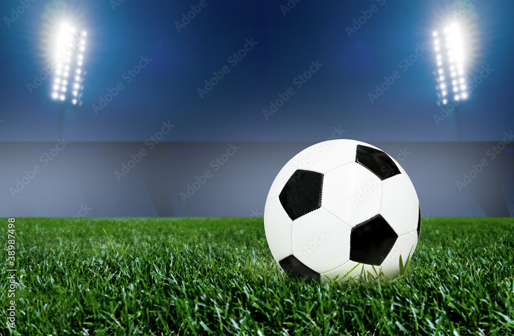 Fototapeta premium Soccer ball on grass field with spotlights