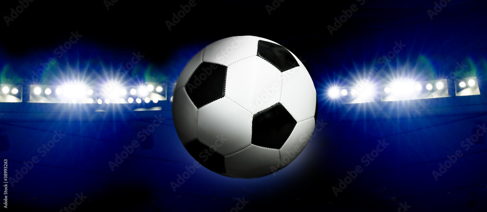 Fototapeta premium Soccer ball and illuminated stadium at night