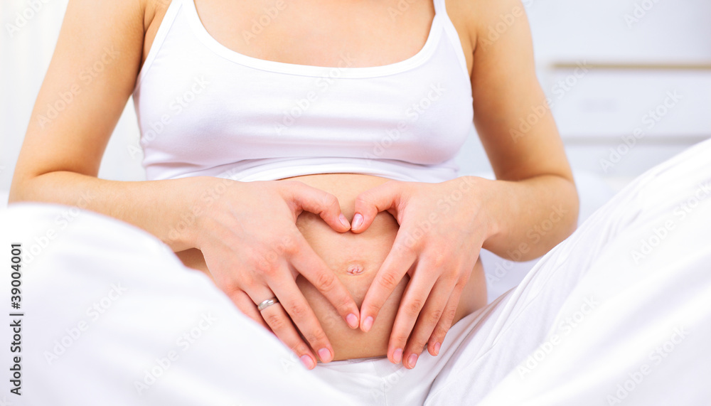 Pregnant woman making heart shape with hands over her stomach Pregnant woman making heart shape with hands over her stomach