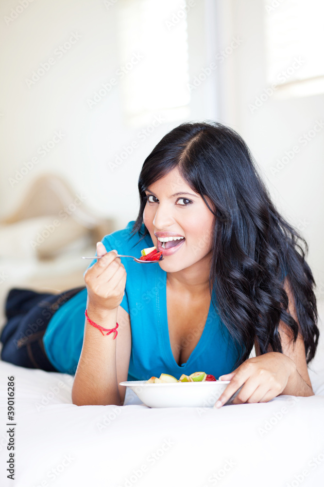 beautiful young woman lying on bed and eating fruit salad beautiful young woman lying on bed and eating fruit salad