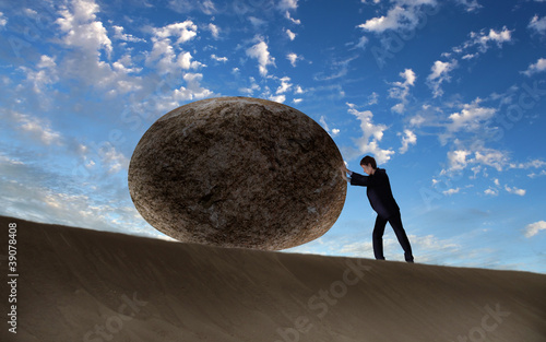 Businessman rolling a giant stone photo