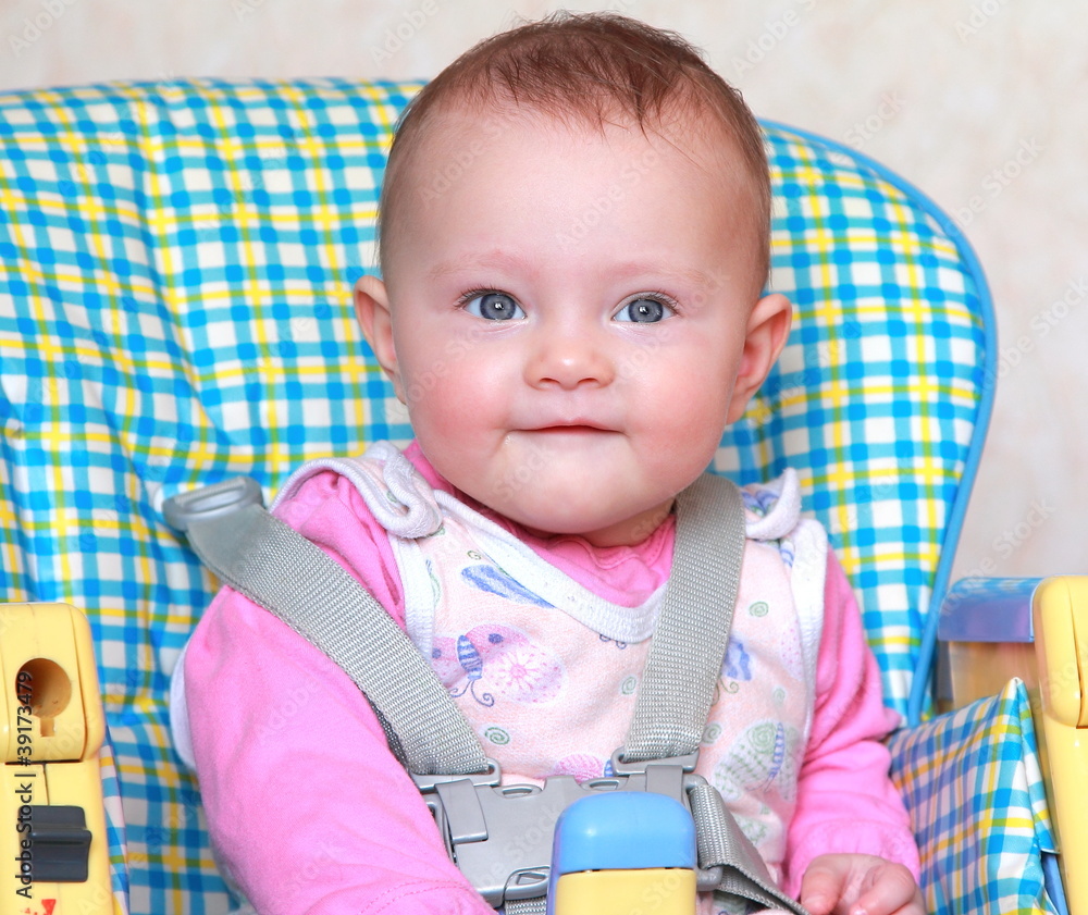Aborable happy baby girl sitting on the bright baby chair and sm Aborable happy baby girl sitting on the bright baby chair and sm