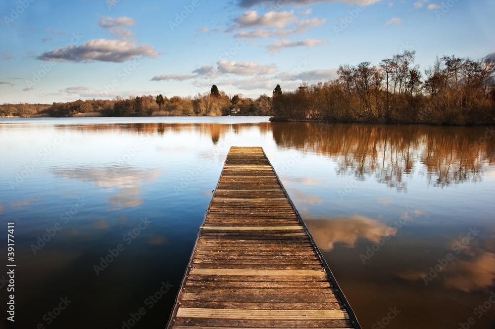 Landscape of fishing jetty on calm lake at sunset with reflectio