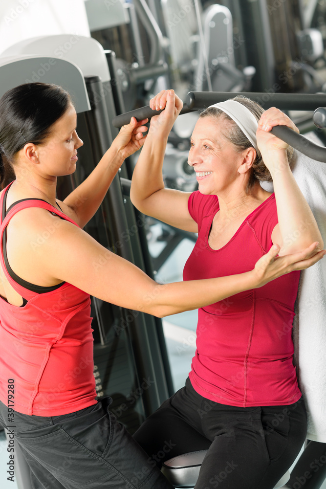 Personal trainer assist senior woman at gym