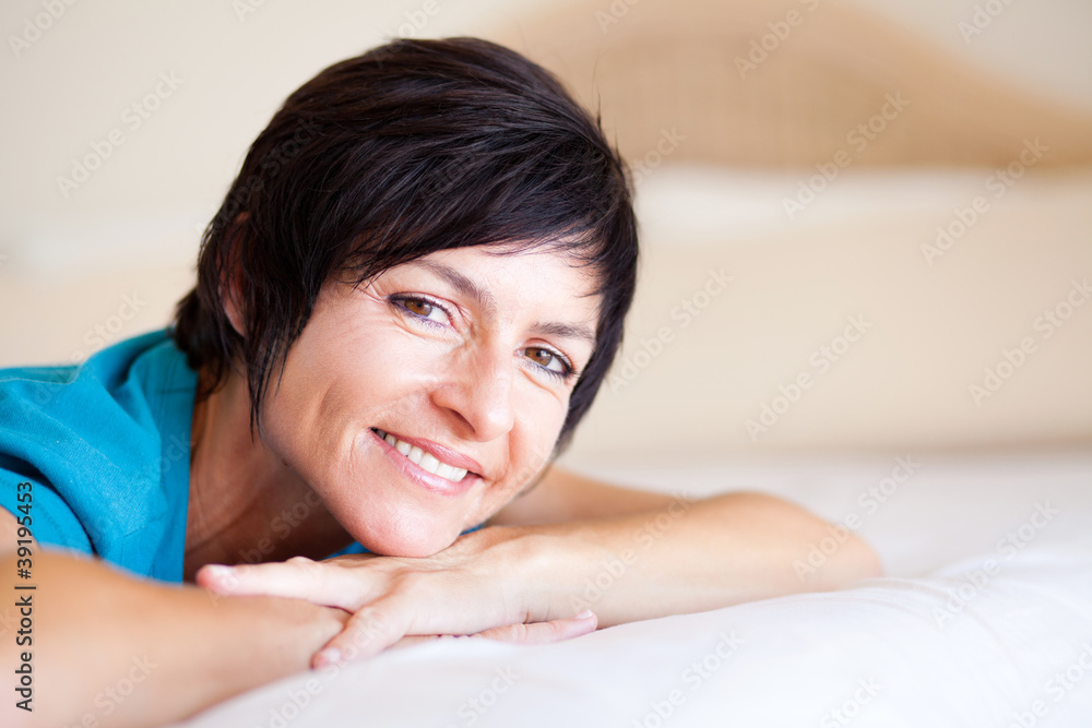 smiling middle aged woman lying on bed relaxing smiling middle aged woman lying on bed relaxing