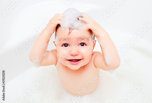 Happy child washing in a bathroom in foam