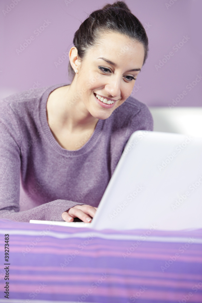Portrait of a young female relaxing in bed while using laptop Portrait of a young female relaxing in bed while using laptop