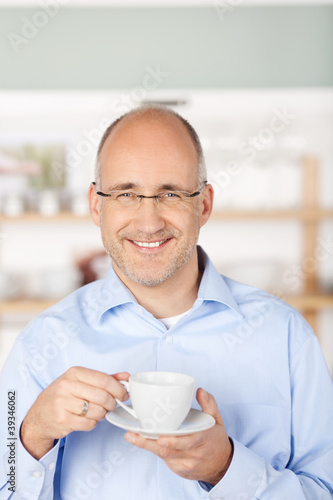 lächelnder mann steht mit einer tasse kaffee in der küche