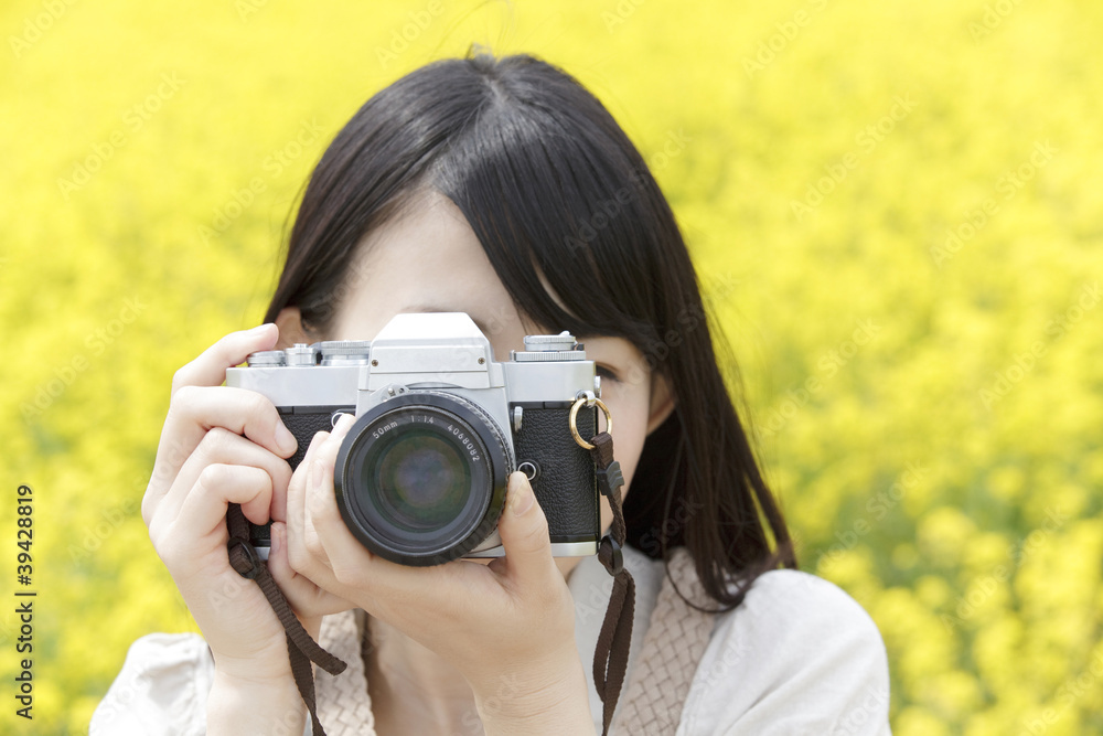 菜の花畑でカメラを構える笑顔の女性
