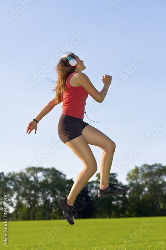 Happy girl listening music jumping in park, enjoying in music © -Marcus-