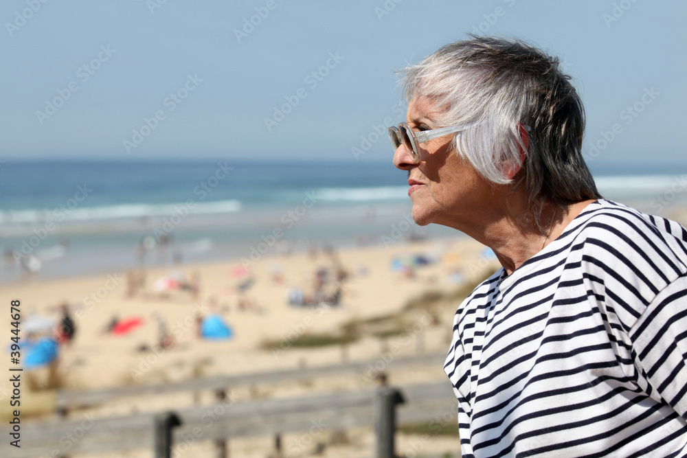 Senior woman looking out over a sandy beach on a summer day