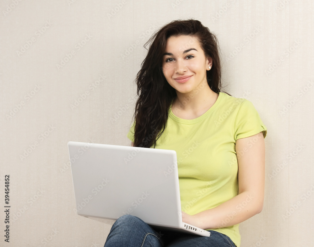 Naklejka premium Young woman sitting with laptop near wall