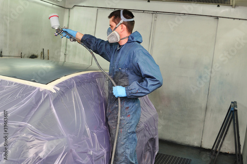 Worker painting a car roof in a paint booth.