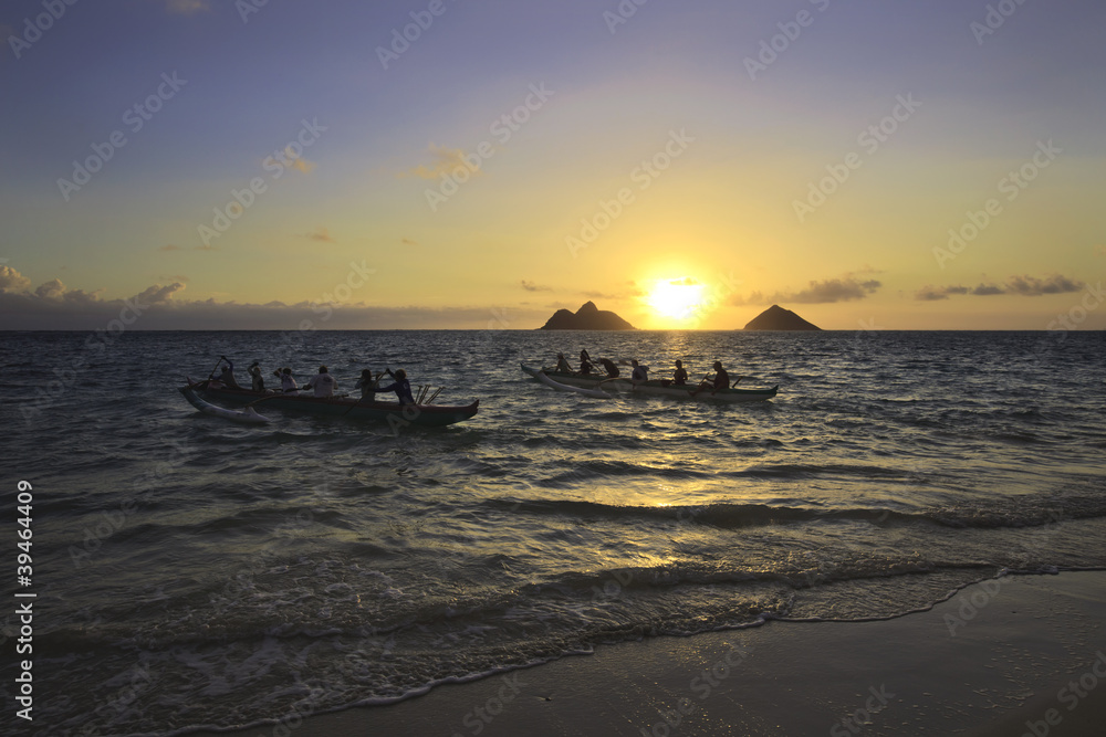 Obraz premium outrigger canoes paddle out from shore at sunrise