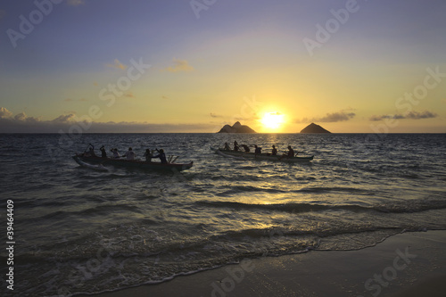 outrigger canoes paddle out from shore at sunrise