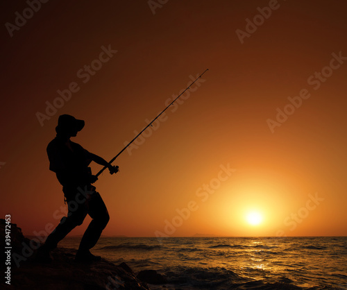 Young fisherman fishing with sunset in the background